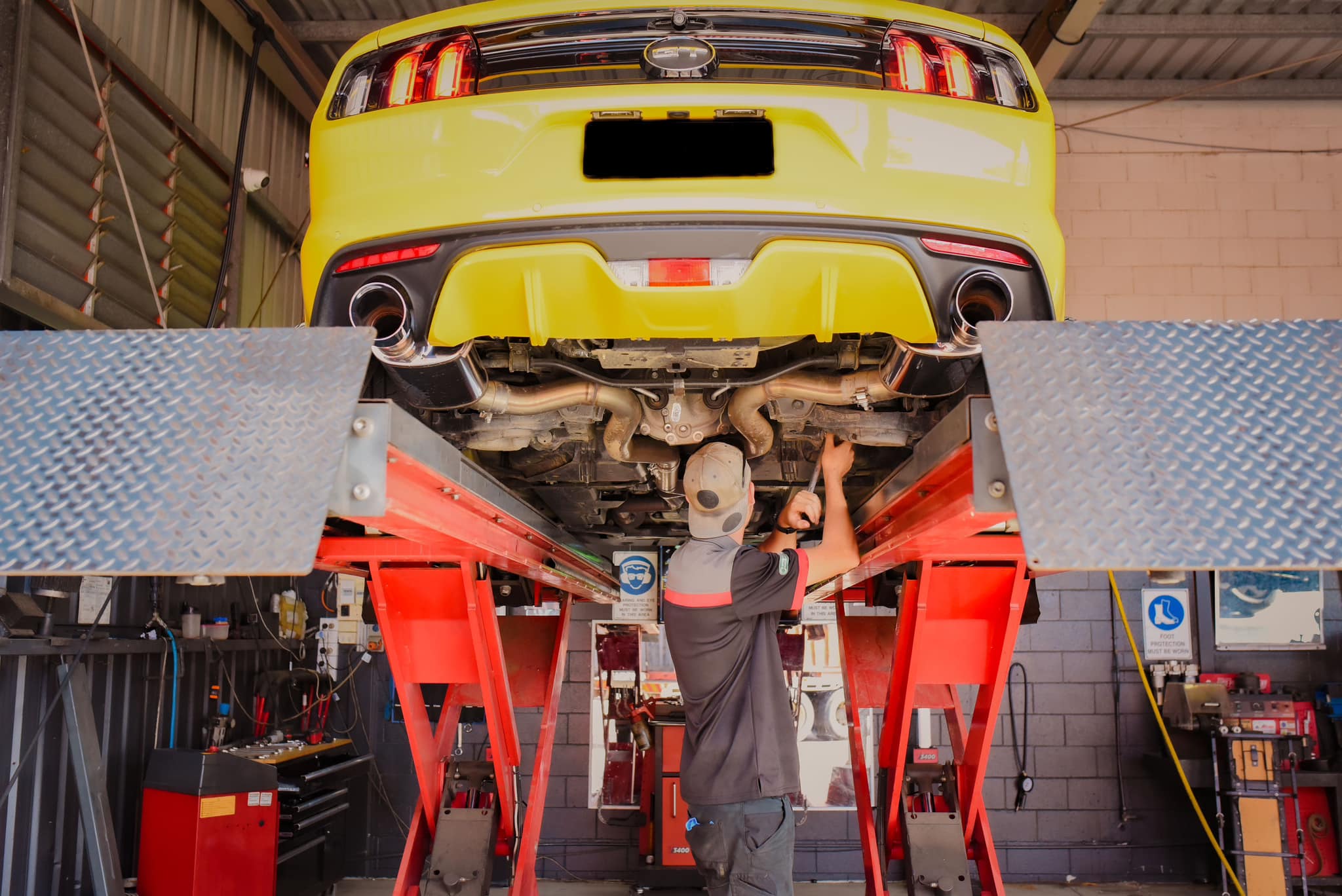 Townsville mechanic working under a yellow Mustang on the hoist at Castle Mechanical in Garbutt
